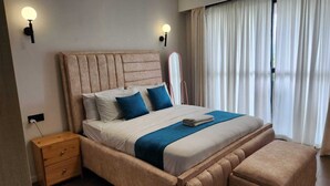 Une chambre à coucher avec un lit, des tables de chevet, une commode, un miroir et une fenêtre avec des rideaux.