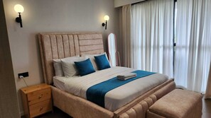 A bedroom with a bed, bedside tables, a nightstand, a mirror, and a window with curtains.