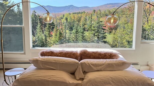 Une chambre à coucher avec un lit, deux lampes de chevet et une grande fenêtre donnant sur les montagnes.