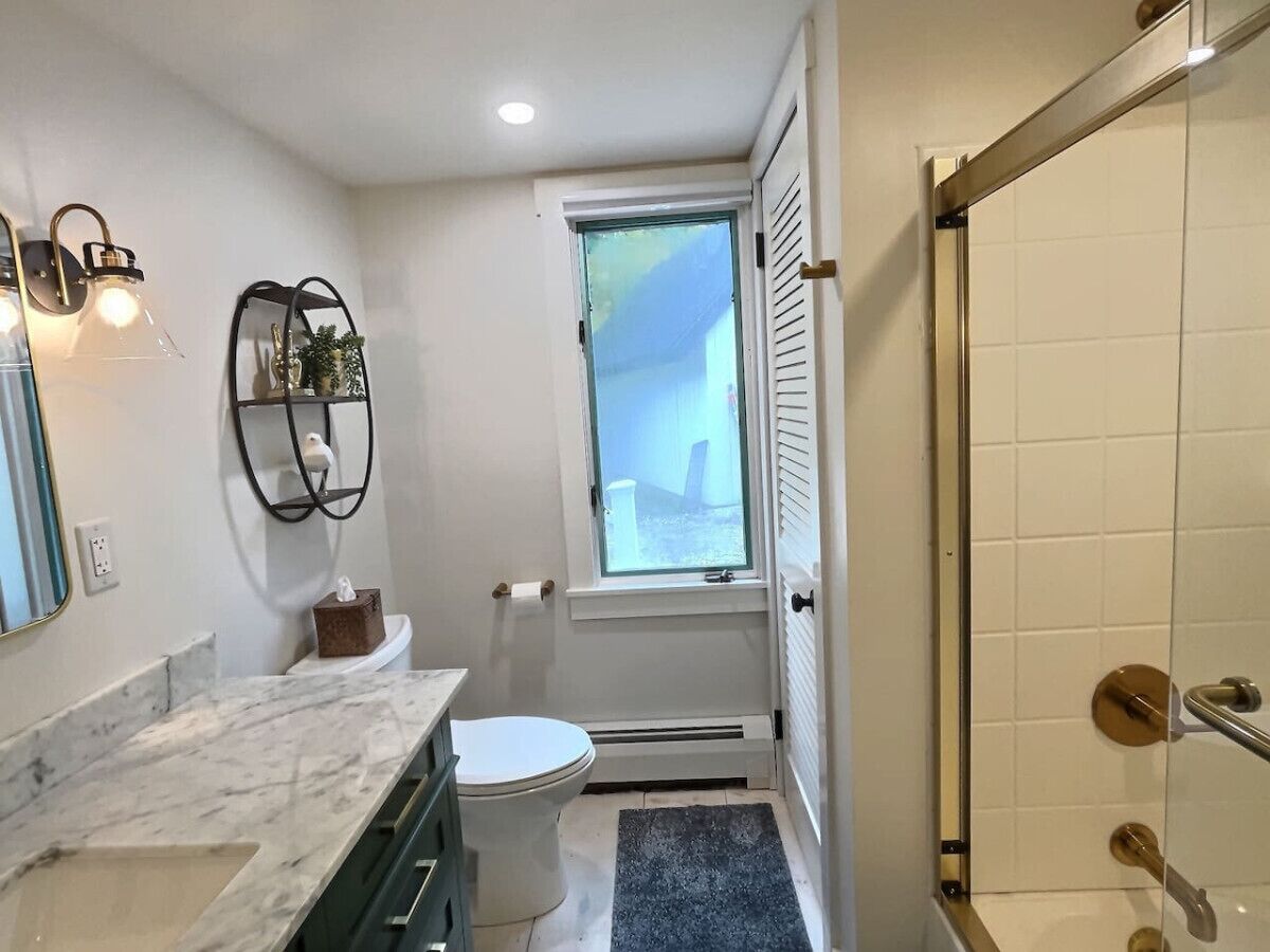 A compact bathroom with a toilet, a small window, a shower area, and a marble countertop.