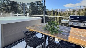 Une terrasse avec un jacuzzi, une table en bois et un barbecue.
