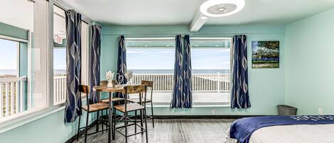 A room with a bed, a table with chairs, a window with curtains, and a painting on the wall.