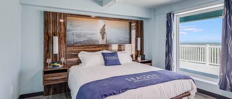 Quarto de hotel moderno com uma cama grande, cabeceira de madeira, vista para o mar e varanda com cortinas.