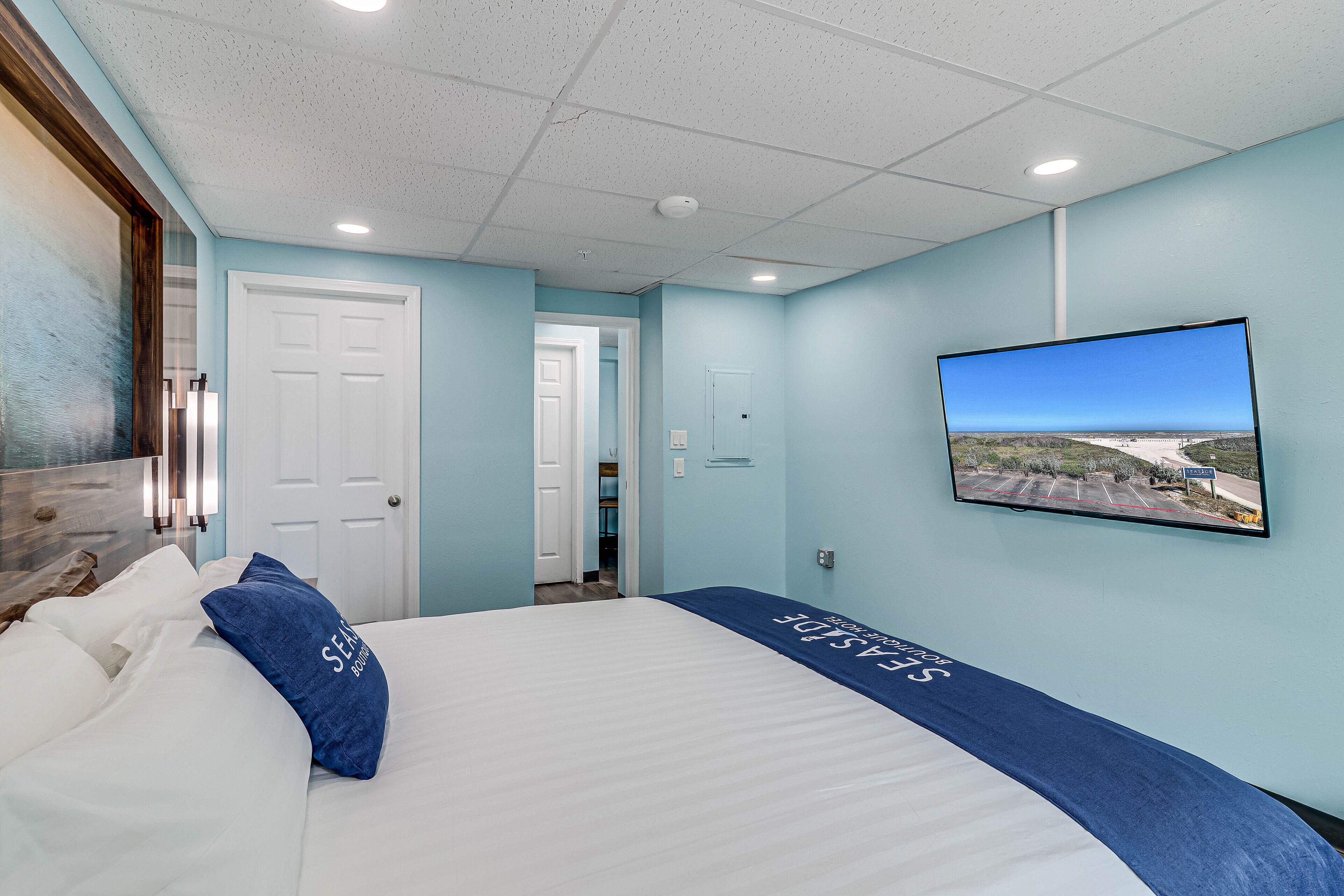 Una habitación de hotel con una cama, un televisor montado en la pared y una puerta que da a otra habitación.