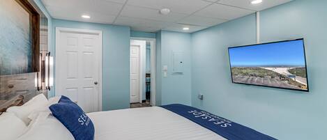 Una habitación de hotel con una cama, un televisor montado en la pared y una puerta que da a otra habitación.