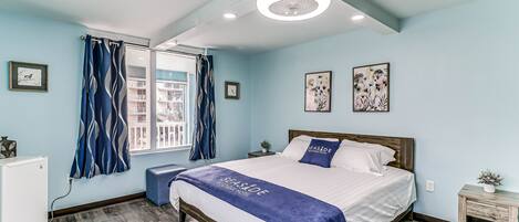 A bedroom with a bed, a bedside table, a small desk, and a window with curtains.