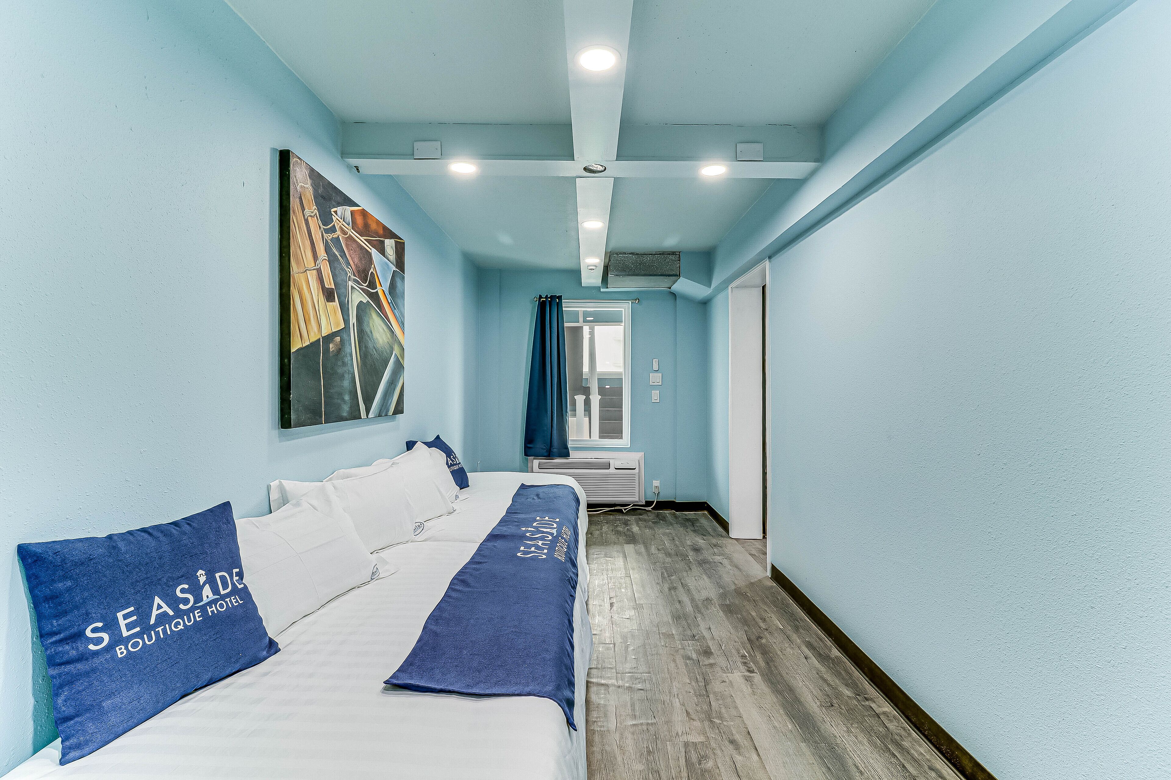 Una habitación de hotel con una cama, una manta azul y un cuadro en la pared.
