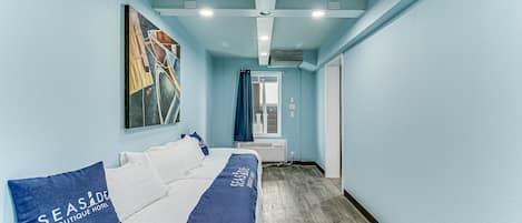 Una habitación de hotel con una cama, una manta azul y un cuadro en la pared.