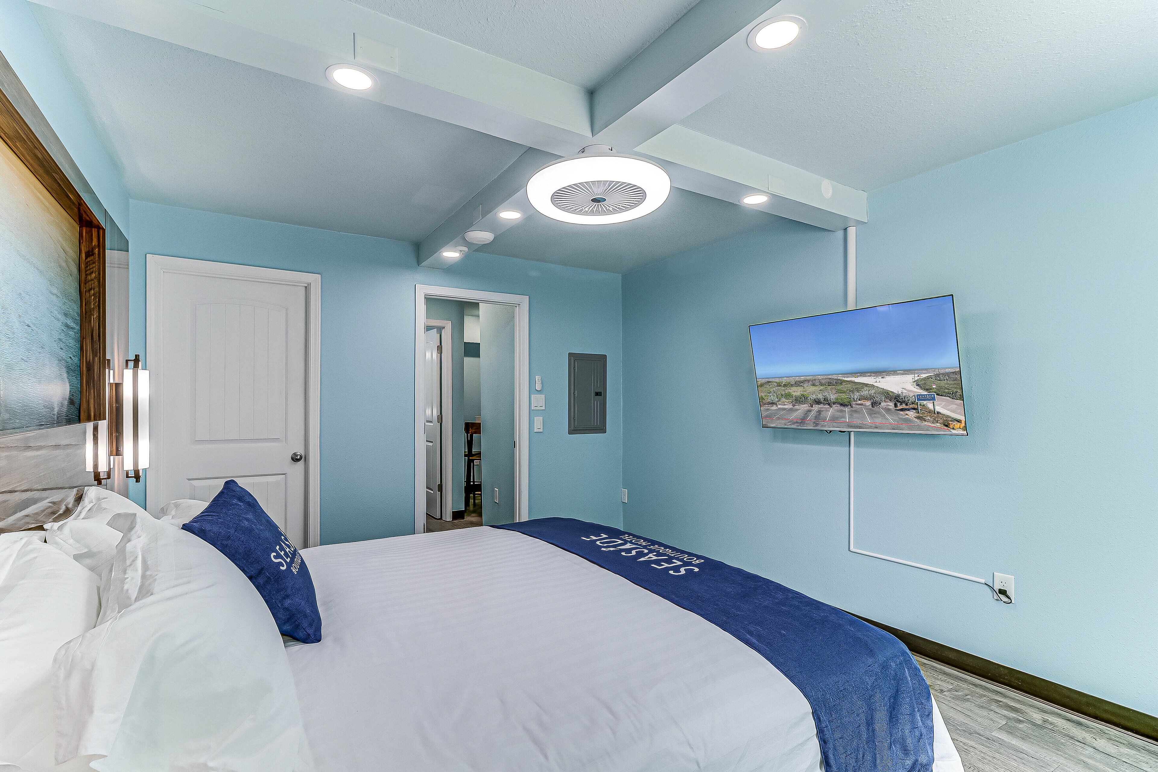A hotel room with a bed, a television mounted on the wall, and a door leading to another room.