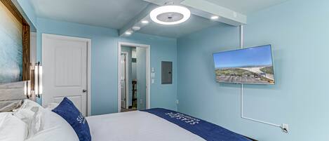 A hotel room with a bed, a television mounted on the wall, and a door leading to another room.