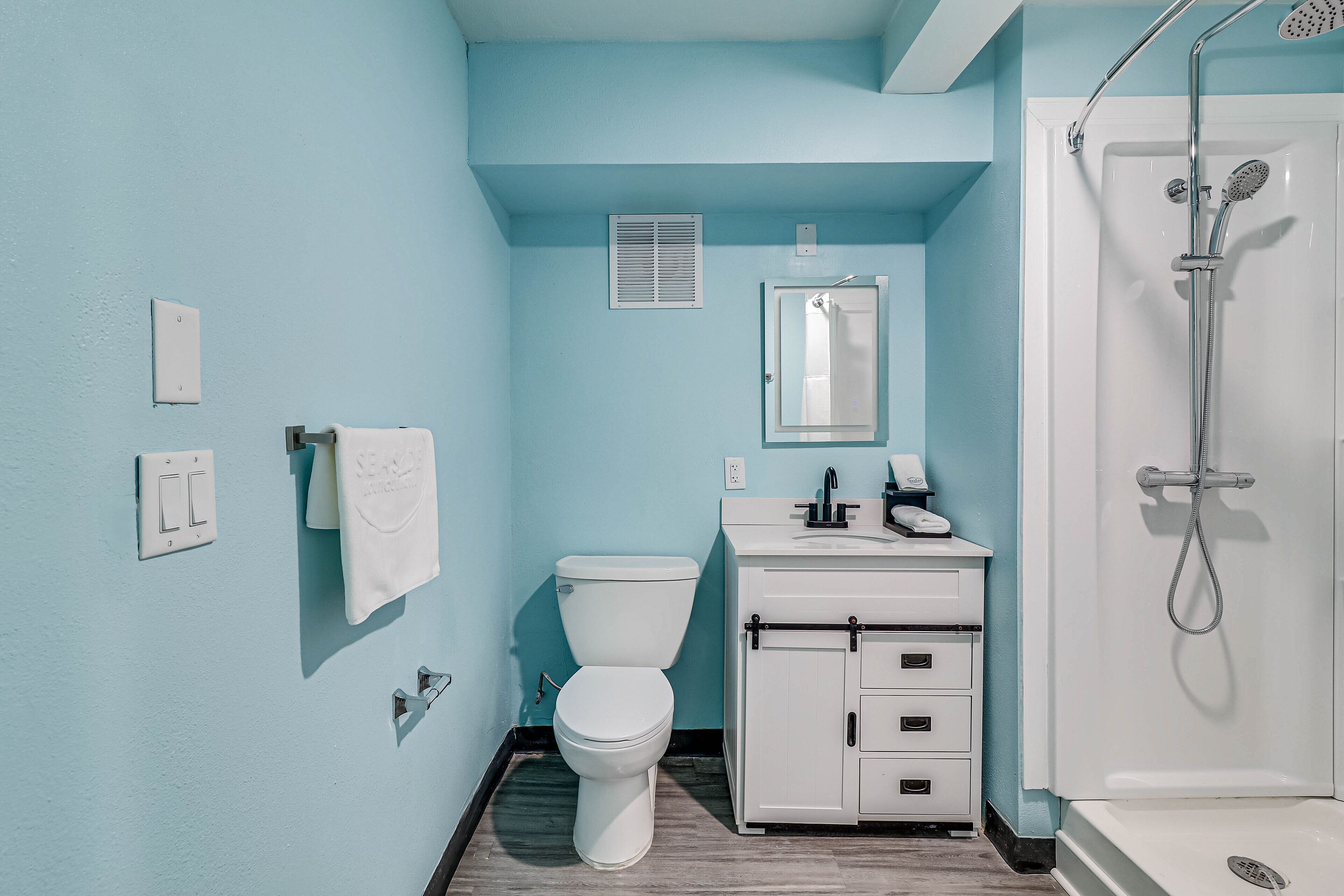 A bathroom with a toilet, sink, mirror, and shower.