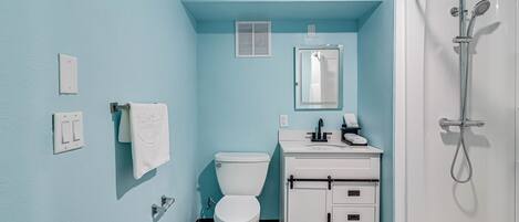 A bathroom with a toilet, sink, mirror, and shower.