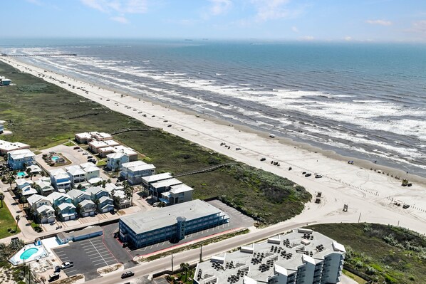 Une vue aérienne d’une zone côtière comprenant une plage, un parking et plusieurs bâtiments.