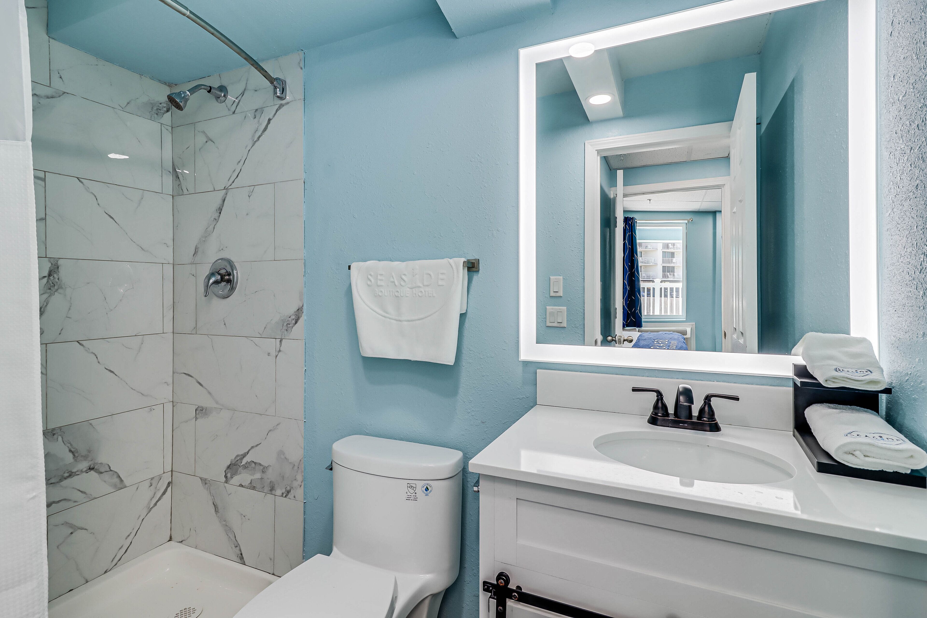 A bathroom with a shower, toilet, sink, and a large mirror.