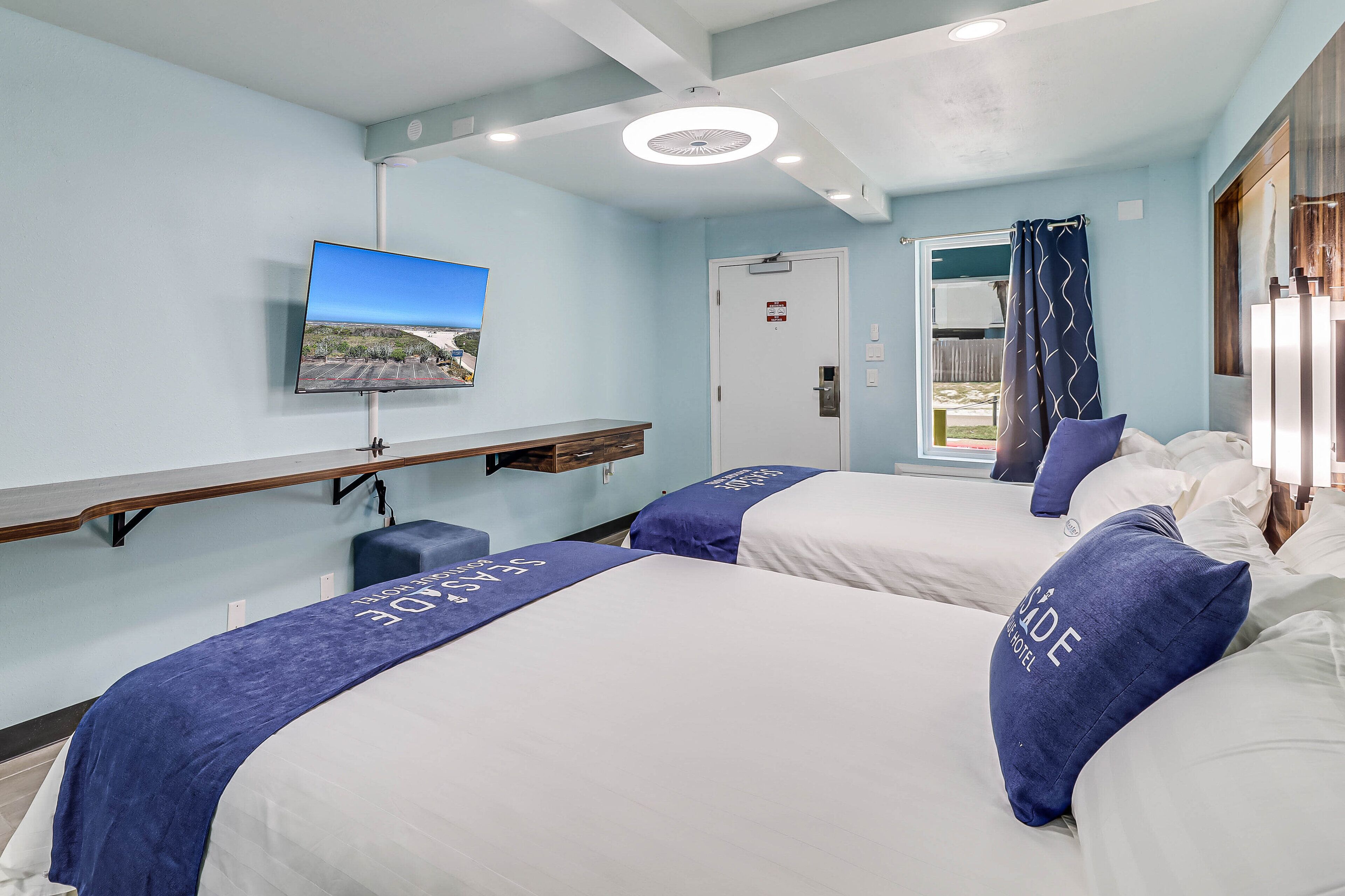 A hotel room with two beds, a TV, a window with curtains, and a door.