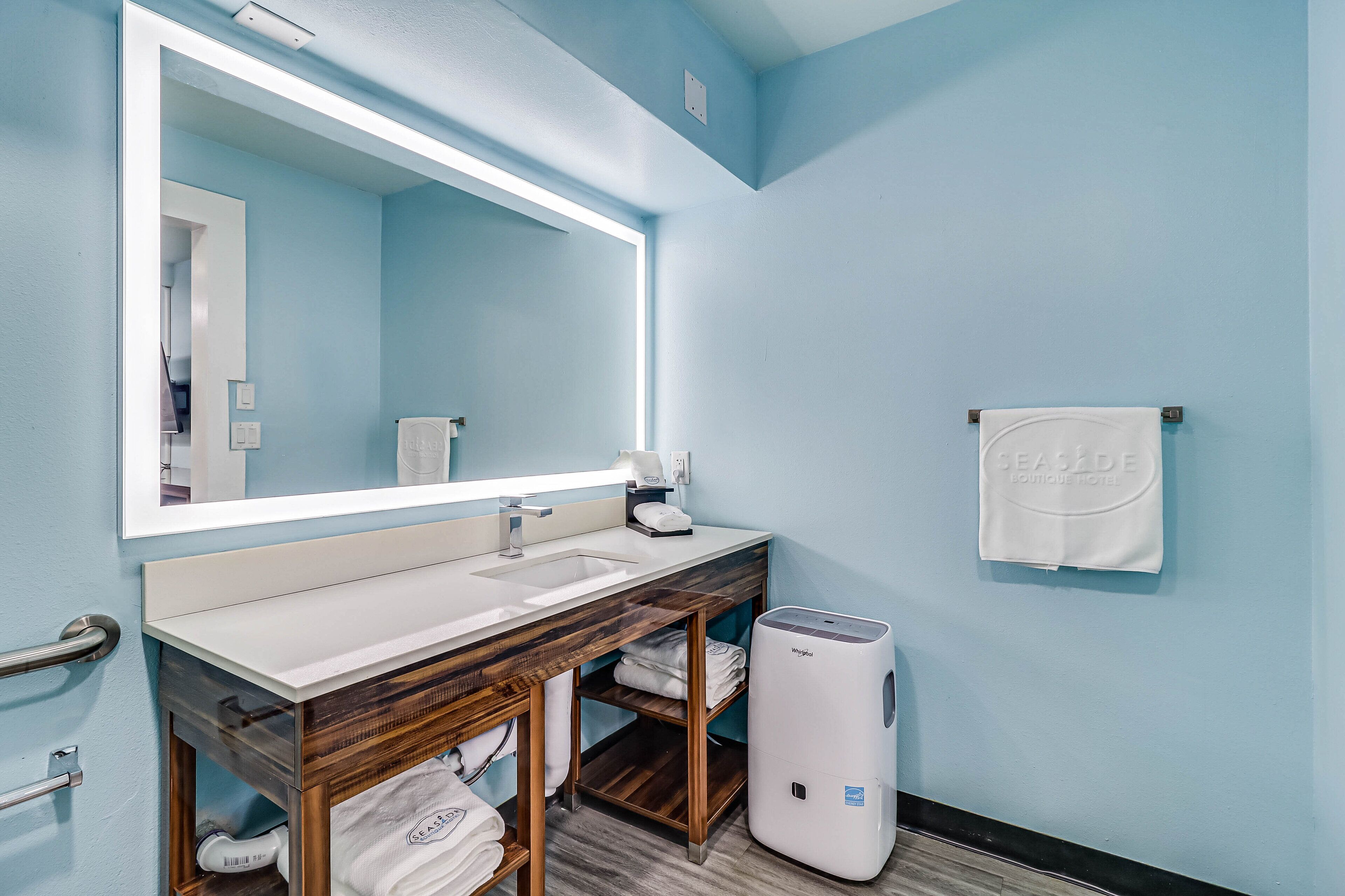 A bathroom with a double sink, wooden vanity, a large mirror, a towel rack, and a hand dryer.