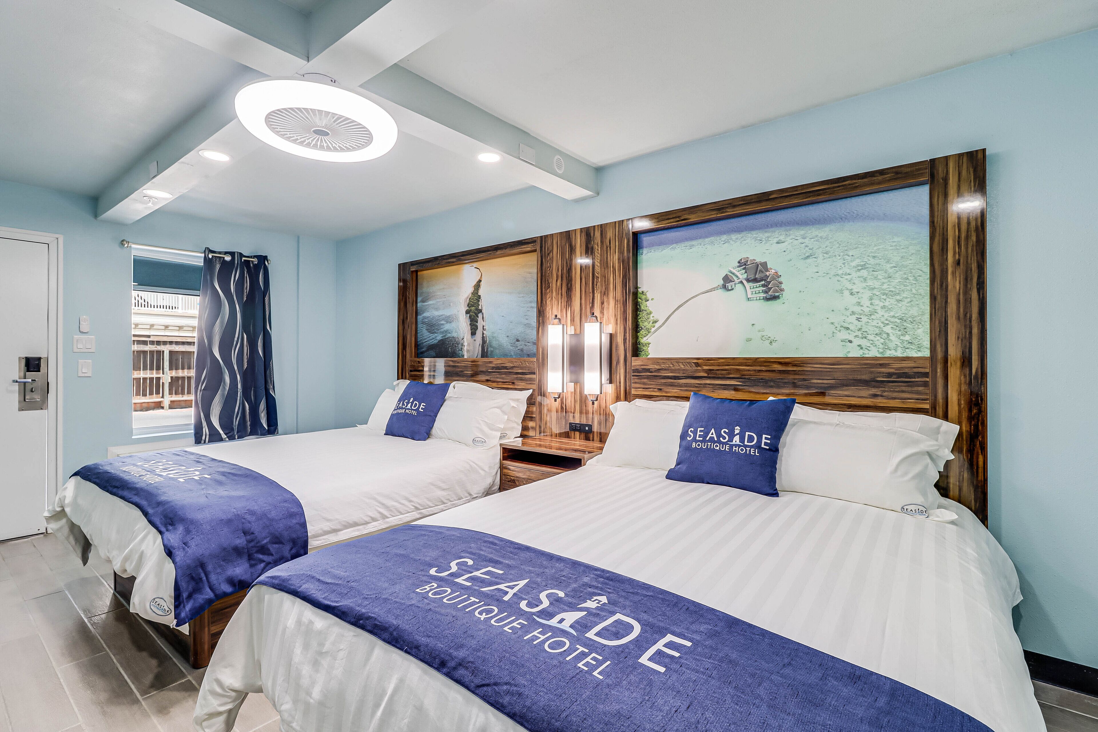 Habitación de hotel con dos camas, cada una con cubrecama azul y blanco, cabecero de madera y un cuadro grande enmarcado sobre las camas.