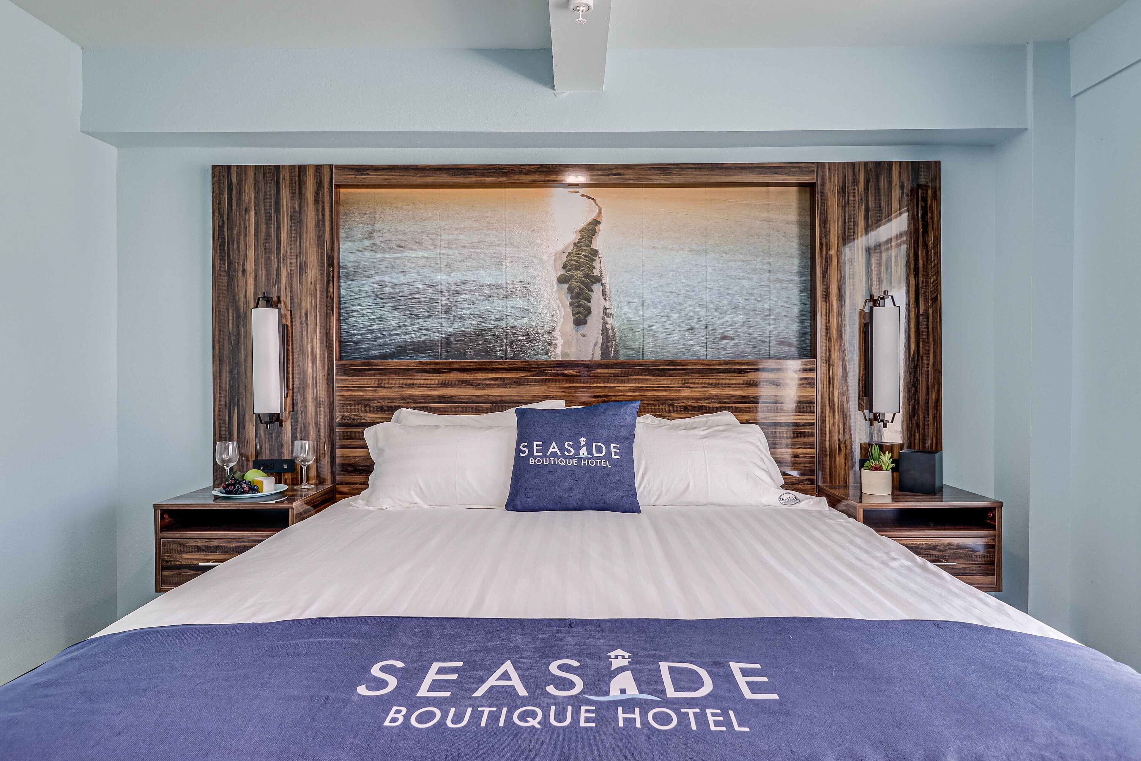 A hotel room with a large bed, wooden headboard, and a painting of a beach scene.