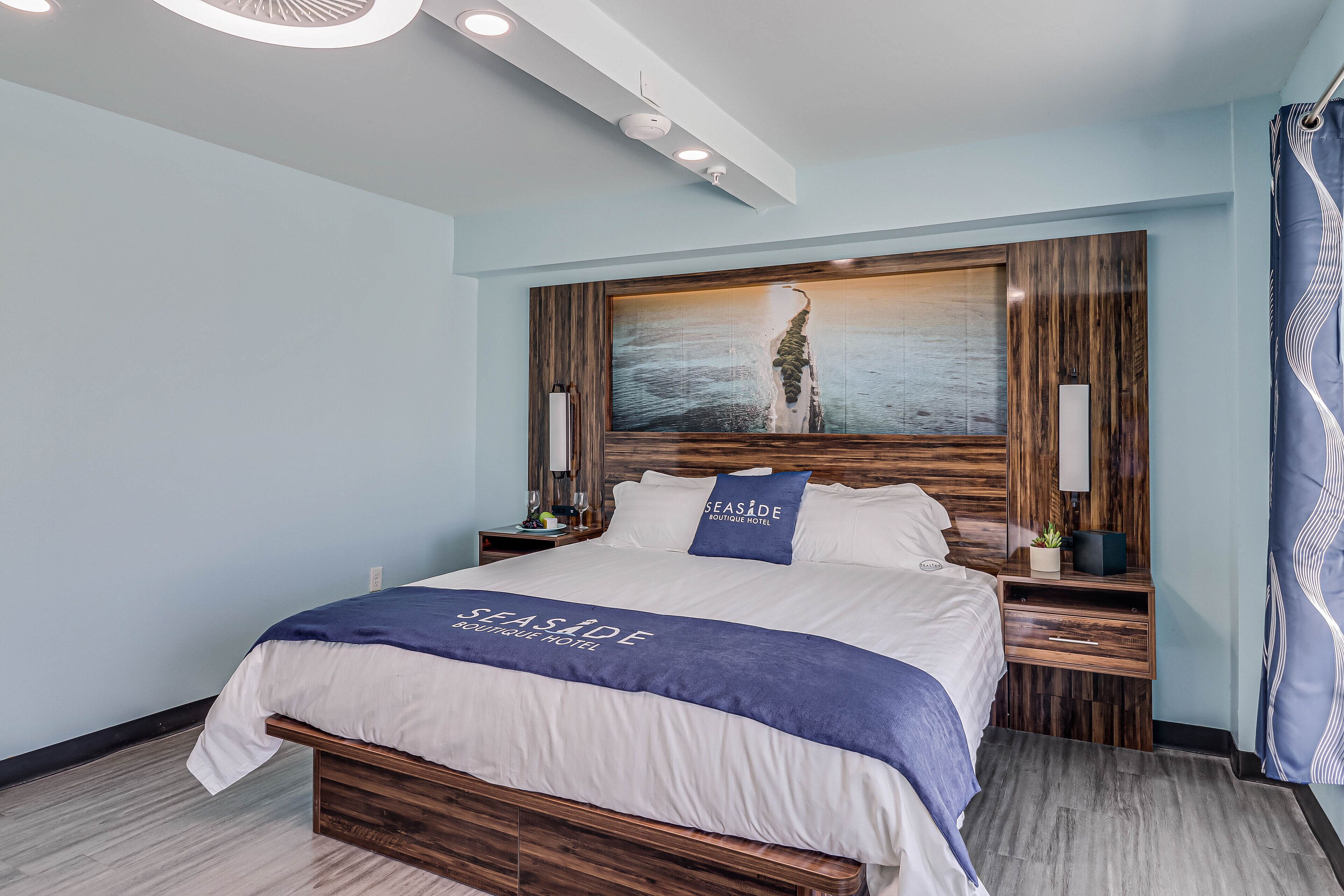 A hotel room with a large bed, wooden headboard, and a painting of a person on a beach.