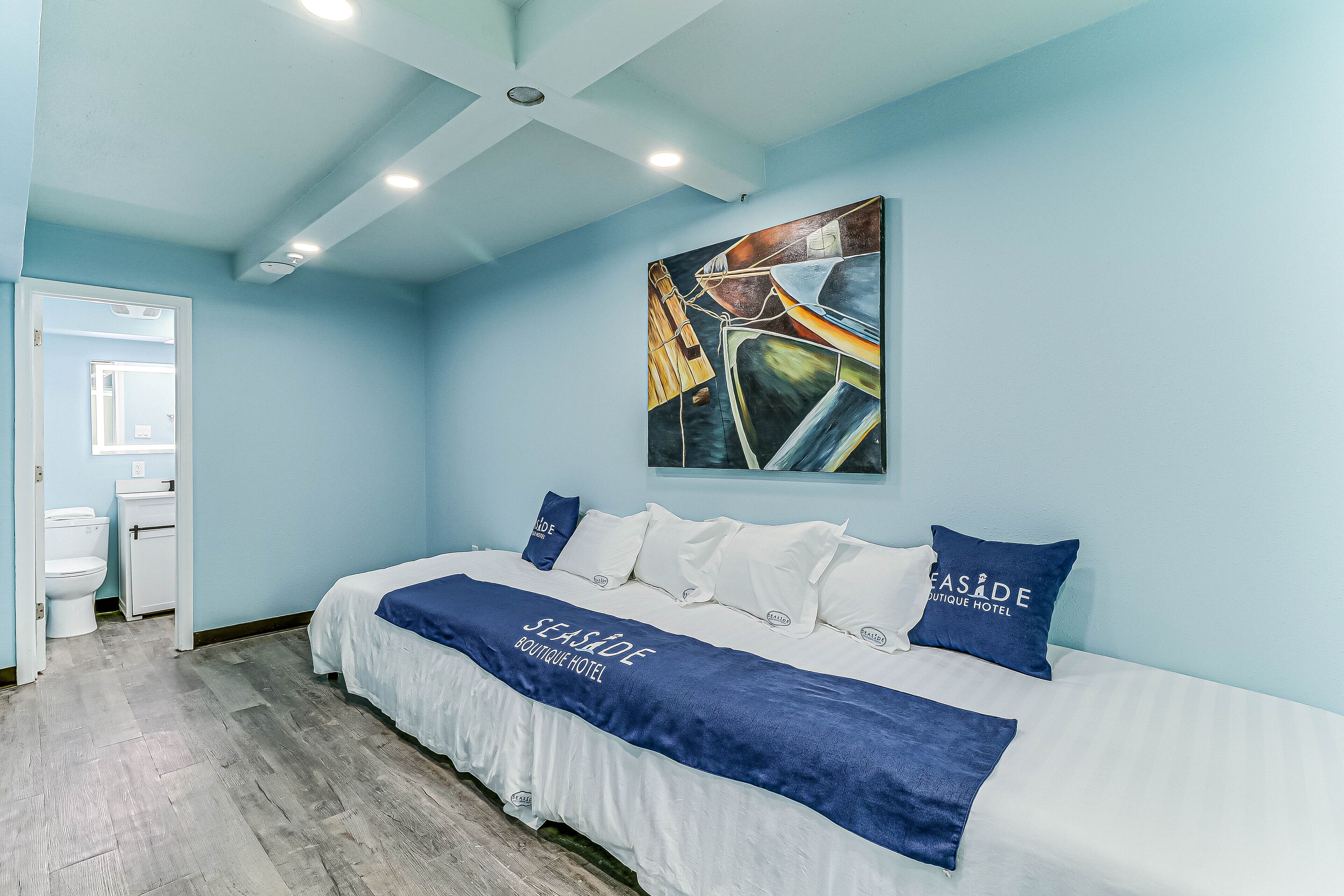 Una camera d'albergo con un letto, un quadro appeso al muro e un bagno visibile attraverso una porta aperta.