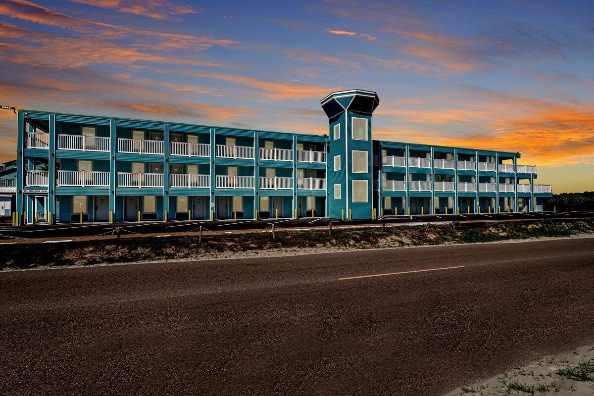 Un motel de varios pisos con balcones y una torre central, situado al lado de una carretera.