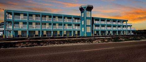 Un motel de varios pisos con balcones y una torre central, situado al lado de una carretera.