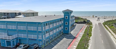Un hotel de varios pisos con fachada azul, estacionamiento y vista a la playa y al océano.