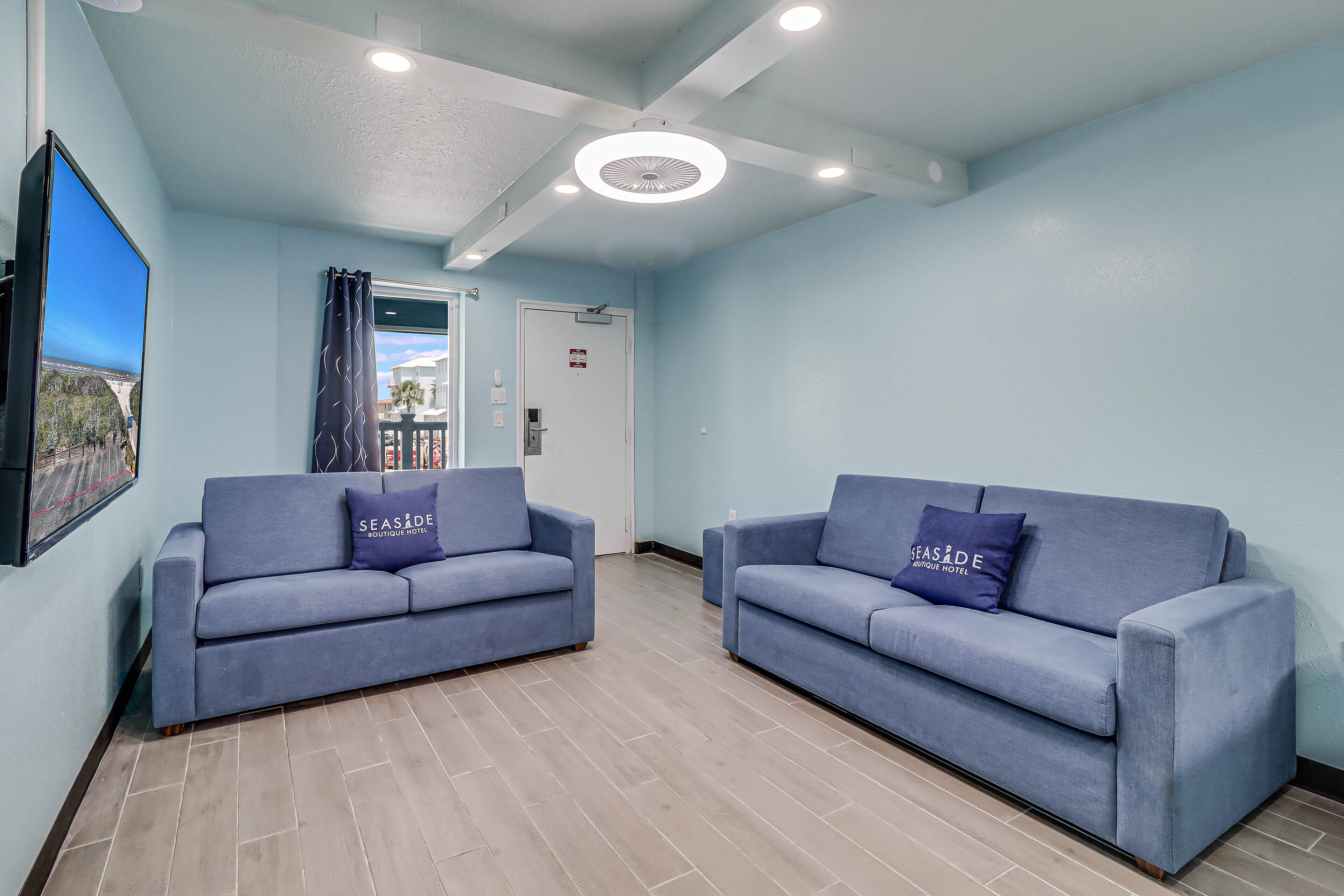 Ein Zimmer mit zwei blauen Sofas, einem Flachbildfernseher und einer Deckenleuchte.