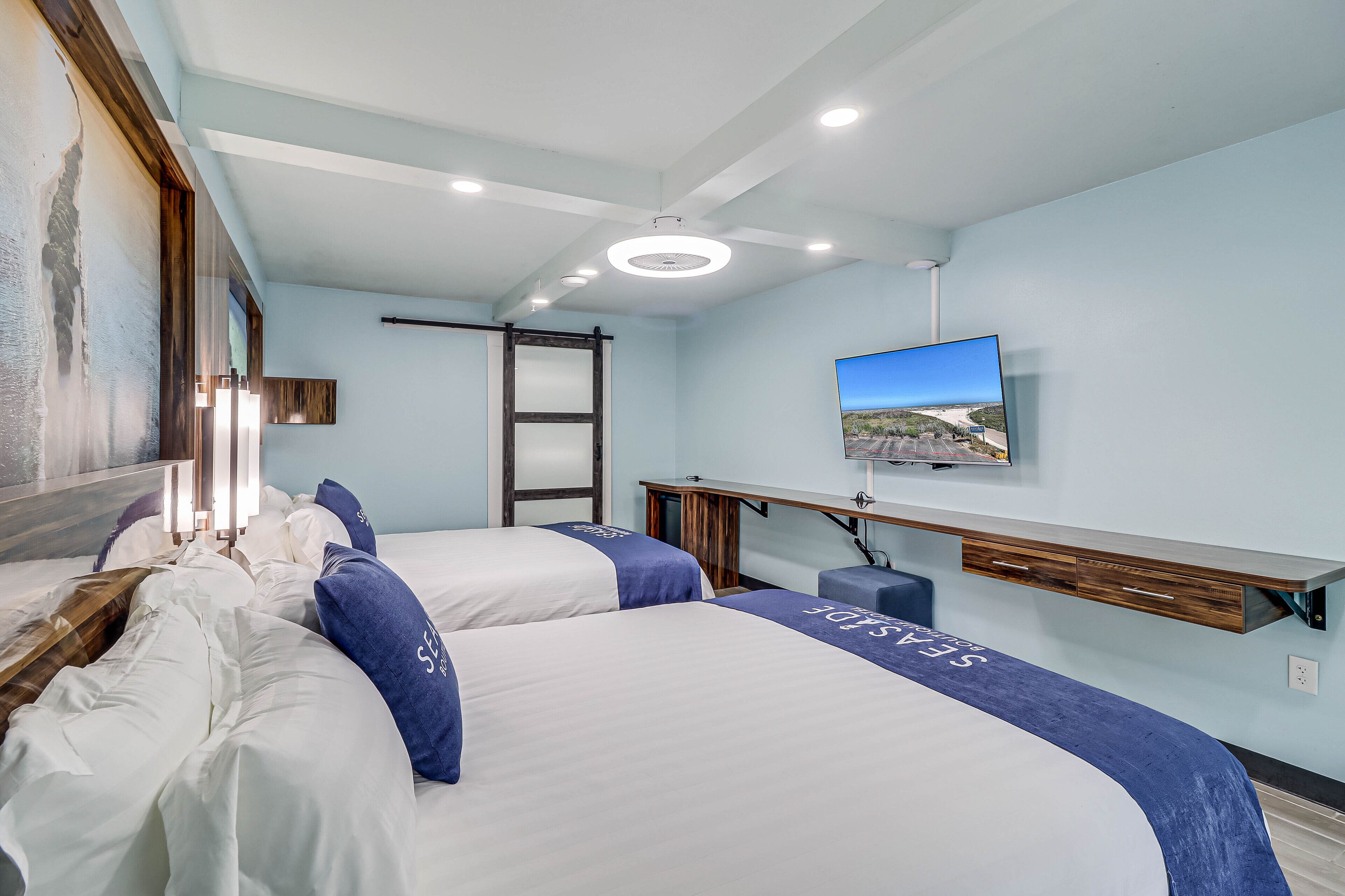 A hotel room with two beds, a desk, a television, and a window with a view.