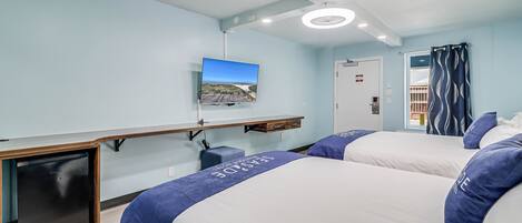Habitació d'hotel amb dos llits, un televisor fixat a la paret, un ventilador de sostre i una finestra amb cortines.