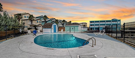 A swimming pool with lounge chairs, a fenced area, and a sunset view.