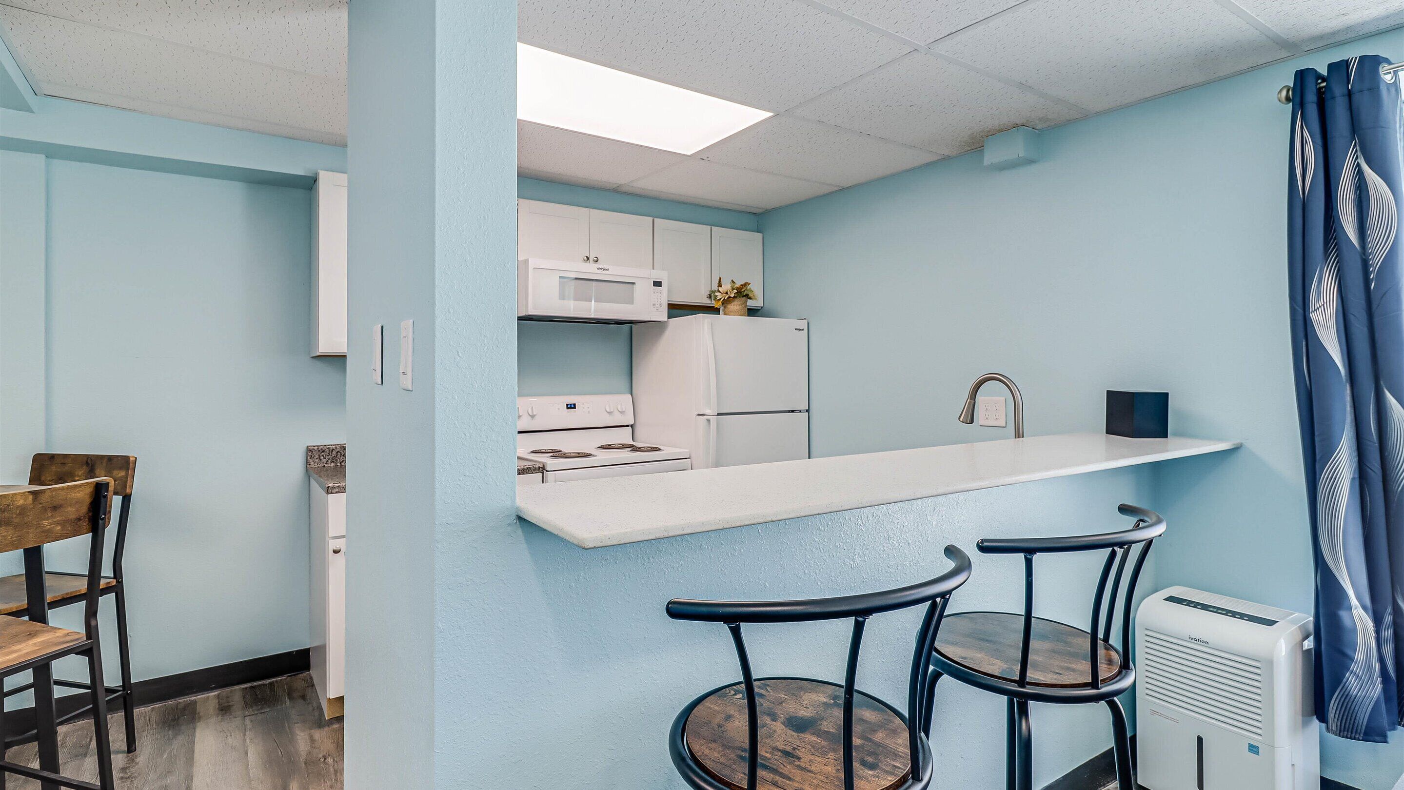 A kitchen with white appliances, a bar counter, and two bar stools.