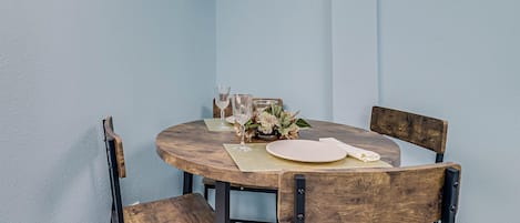 Una mesa redonda de madera con un mantel individual, dos platos blancos, dos copas de vino y un pequeño arreglo floral.