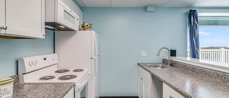 A compact kitchen with white appliances, a granite countertop, and a view of the outdoors.