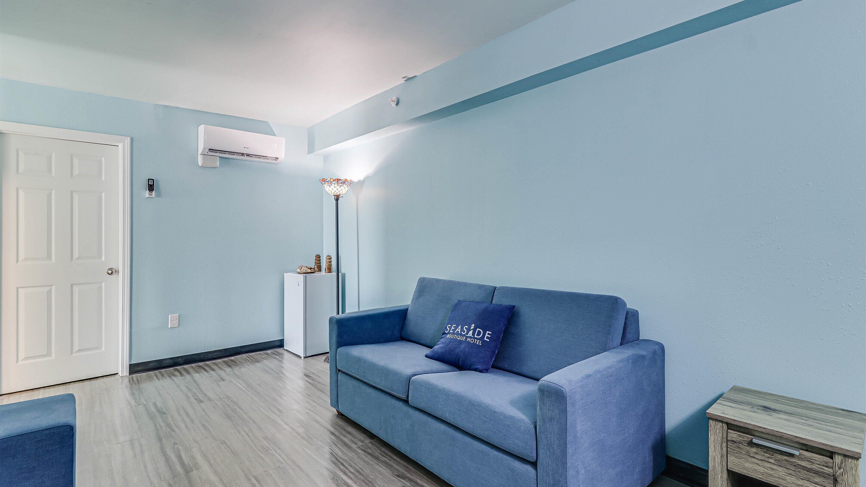 Un salon avec un canapé bleu, une porte blanche et un climatiseur fixé au mur.