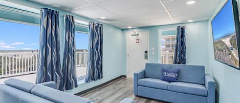 En hotellobby med en blå soffa, en receptionsdisk och stora fönster som erbjuder utsikt över stranden och havet.