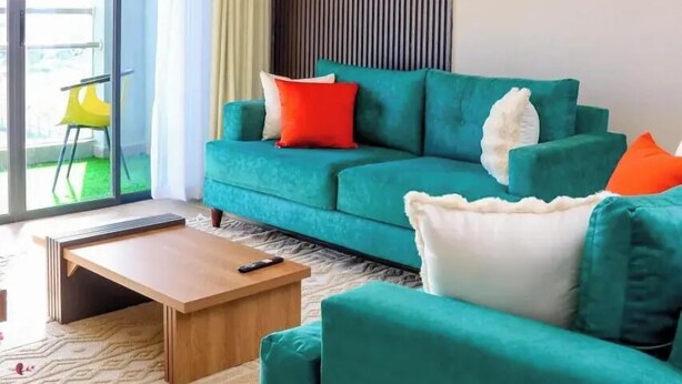 En moderne stue med en turkis sofa, et træ sofabord og en skydedør, der fører ud til en balkon med en gul stol.