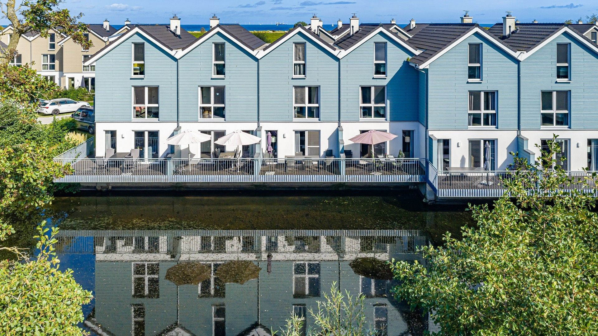 A row of light blue buildings with balconies, a canal in the foreground, and a clear sky.