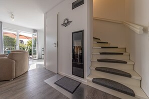 Un intérieur moderne avec un escalier, une porte ornée d’un motif solaire et un coin salon offrant une vue sur l’extérieur.