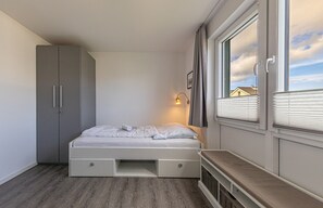 Une chambre à coucher comprenant un lit, une armoire, une table de chevet, une lampe et une fenêtre avec des stores.