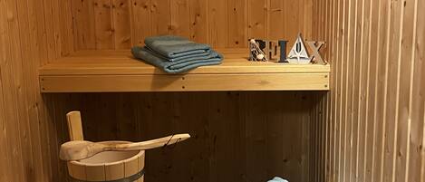 Uma sauna de madeira com um banco, um balde de madeira e toalhas dobradas.