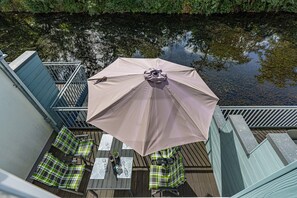 Eine Terrasse im Freien mit Tisch und Stühlen, einem großen Sonnenschirm und Blick auf ein Gewässer.