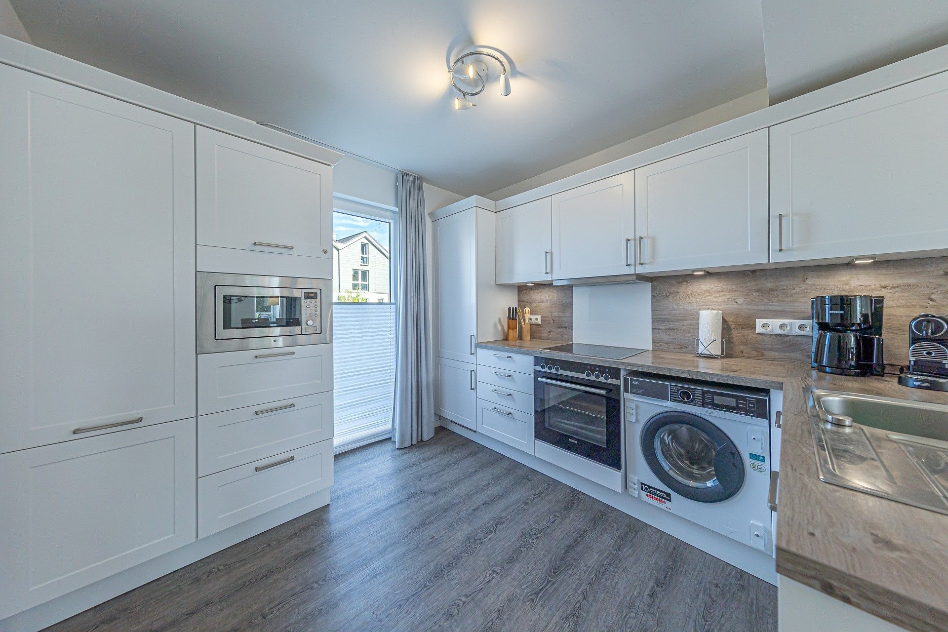 A modern kitchen with built-in appliances, a washing machine, and a coffee maker.