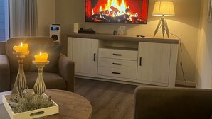 Una sala de estar acogedora con un televisor de pantalla plana sobre la chimenea, una mesita de noche con velas y una lámpara.
