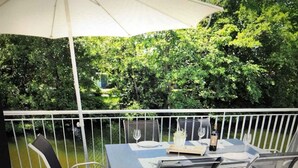 Una terraza con mesa y sillas, una sombrilla blanca, y vistas a un río y vegetación.