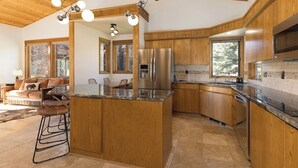 A spacious kitchen with wooden cabinets, a central island, and a large refrigerator. - Lone Moose Lookout | Big Sky Meadow (Big Sky)