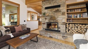 A cozy living room with a stone fireplace, a bookshelf, and a comfortable seating area. - Lone Moose Lookout | Big Sky Meadow (Big Sky)