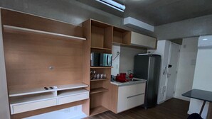 A compact kitchen with built-in appliances, a dining area with a purple chair, and a small table. - Tela de Cinema! Novinho Prox. Paulista c/ Vaga (Consolação São Paulo)