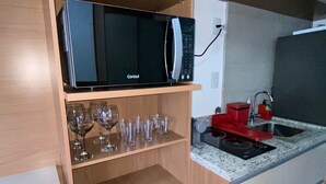 A kitchen with wooden cabinets, a microwave, a red kettle, and wine glasses on shelves. - Tela de Cinema! Novinho Prox. Paulista c/ Vaga (Consolação São Paulo)