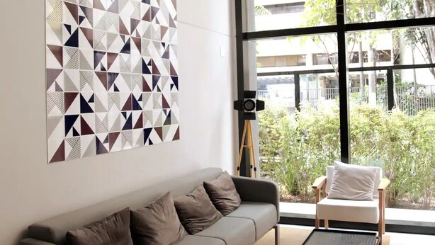 A modern living room with a gray sofa, a white armchair, and a small table. There is a large window with a view of buildings and trees. - Tela de Cinema! Novinho Prox. Paulista c/ Vaga (Consolação São Paulo)
